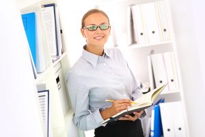 Portrait of a smiling bookkeeper standing by the shelves